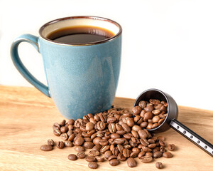 Coffee beans spilling from a scoop with a green mug of coffee