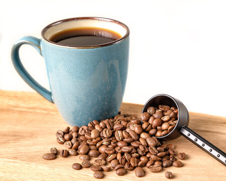 Coffee beans spilling from a scoop with a green mug of coffee