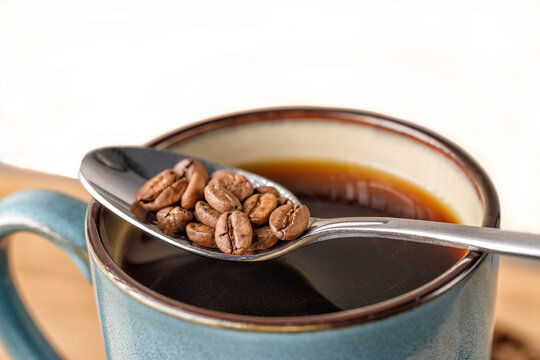 Coffee beans in a spoon balanced over a green mug of coffee