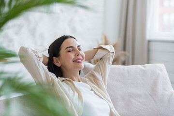 Close-up photo of a young beautiful woman relaxing at home with her eyes closed, her hands behind...