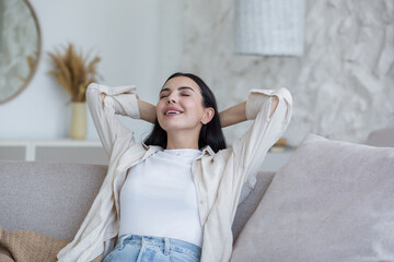 Close-up photo of a young beautiful woman relaxing at home with her eyes closed, her hands behind...