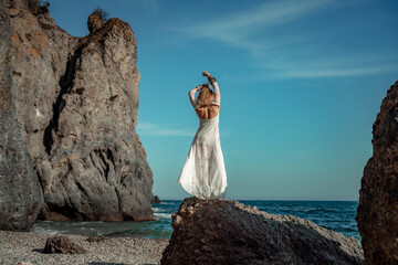 Middle aged woman looks good with blond hair, boho style in white long dress on the beach...