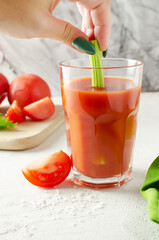 One transparent glass glass with red tomato juice and a woman's hand holds a sprig of celery. Healthy food concept. Vertical orientation. Selective focus.