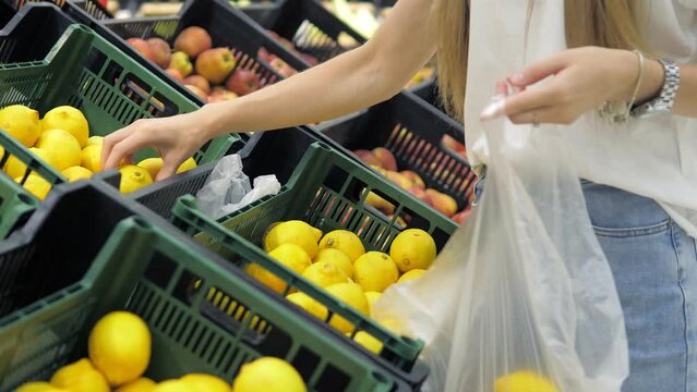 A beautiful young girl in close-up chooses a lemon in the supermarket and collects it in a pocket. People buy food in a store, a hypermarket. Grocery store shelves.Bakery department.Healthy food
