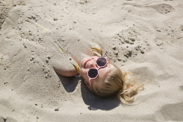 Cute happy little girl buried in the sand on the beach.