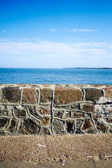 Stone wall separating the pier from the sea against the background of the blue sky and the sea.