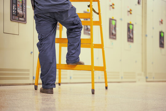 Electrician worker with wooden ladder on electrical cabinets background
