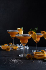 Glasses of orange cocktail decorated with orange and sugar on the edge of glass on black background