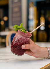 Personne tenant un cocktail rouge avec une paille dans la main