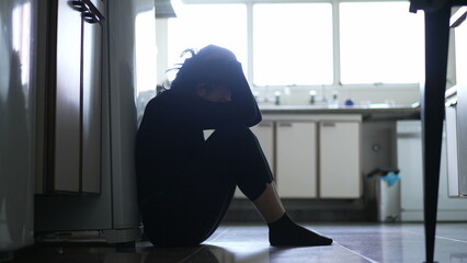 Silhouette of depressed woman sitting on kitchen floor. Sad person lonely and unhappy