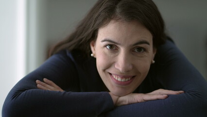 Fototapeta premium Portrait of woman in her 30s smiling at camera leaning on table with arms crossed closeup face