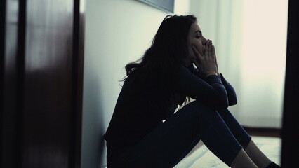 Desperate person in distress during emotional crisis. Woman sitting on floor at home feeling ashamed. Depressed girl alone - obrazy, fototapety, plakaty