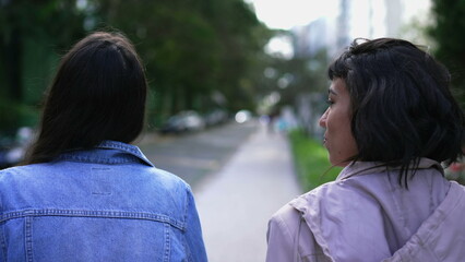Obraz premium Back two young women walking outside together. Two female friends chatting