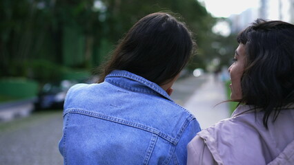 Fototapeta premium Back two young women walking outside together. Two female friends chatting