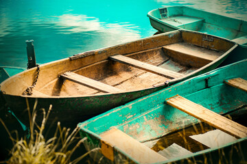 Fototapeta na wymiar Old turquoise fishing boats float near the shore on the river surface of the water on a clear summer day. Summer vacation. Fishing.