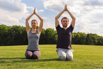 Young healthy couple doing yoga in the sunny summer park. Fitness and healthy lifestyle