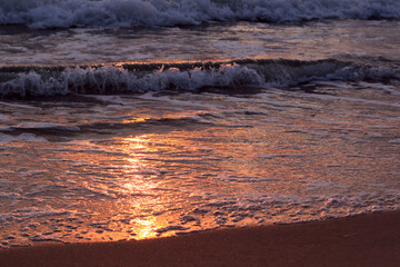 foamy waves on the beach and golden sunset reflection