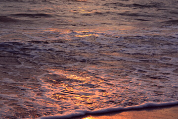 Fototapeta na wymiar foamy waves on the beach and golden sunset reflection