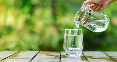 Pour clean water from a jug into a glass placed on a wooden bar.	
