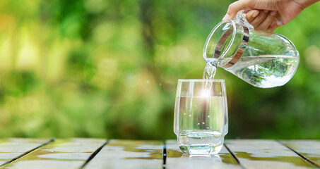 Obraz premium Pour clean water from a jug into a glass placed on a wooden bar. 