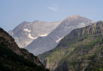 Valle alpino con montañas de color gris con nieve de fondo y cielo azul