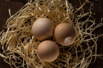 Fresh chicken light brown eggs in a straw nest. Wooden table. Close up.