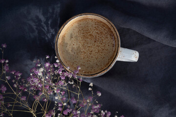 a cup of coffee from above on a background of blue linen fabric and flowers