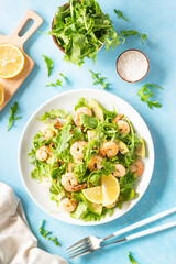 Shrimp salad with arugula, avocado and olive oil at blue table. Vertical image.