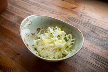 Fresh pickled cabbage in light green bowl on wooden table. Top view