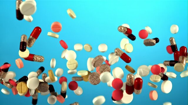 Different types of pills fly up and fall down. On the blue screen. Filmed on a high-speed camera at 1000 fps.