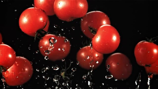 Tomatoes with splashes of water take off and rotate in flight. On a black background. Filmed is slow motion 1000 fps.
