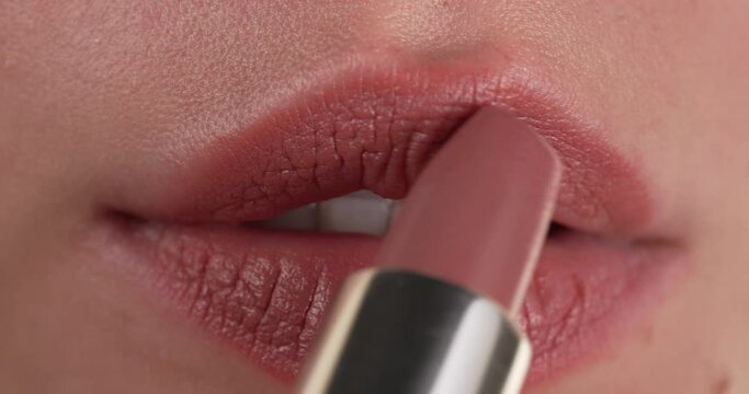 Close up view of a woman applying natural color lipstick on her full lips. Macro. Lips makeup.