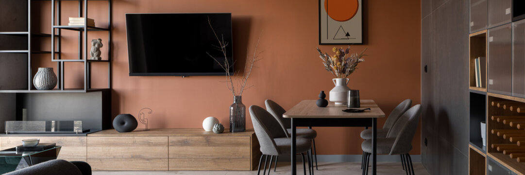 Living room with dining table and rusty colored wall, panorama