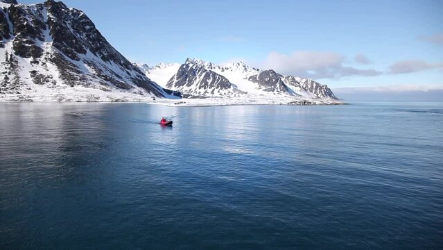 Lancha en movimiento en un mar en calma bajo un cielo azul y monta&ntilde;as nevadas en el archipi&eacute;lago de Spitsbergen, islas Svalbard en noruego