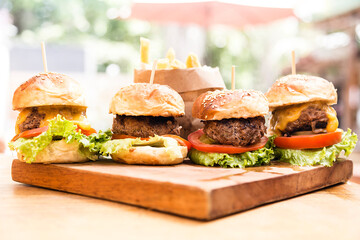 Four hamburgers on a wooden board and french fries served in a wooden paper basket
