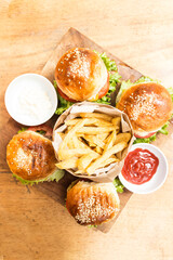 Four hamburgers on a wooden board and french fries served in a wooden paper basket