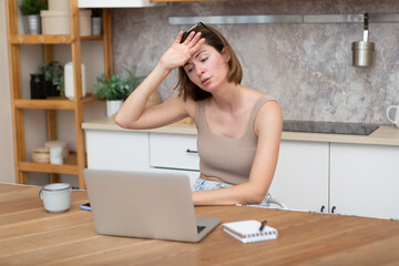 Young attractive woman sitting at the table and working on laptop in the kitchen at home