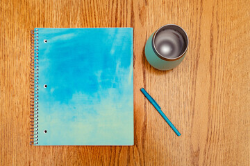 Aqua blue green notebook, pen and cup on a wooden table with a shallow depth of field and copy space