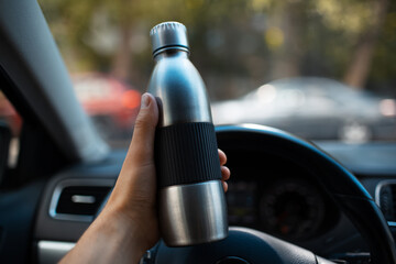 Close-up of male hand holding steel reusable water bottle inside car.