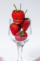 Bright red ripe strawberries in a clear glass, on a macro image, white background.
