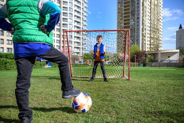 Little preschool boys friends playing soccer football on playground grass field outside. Happy authentic candid childhood lifestyle. Seasonal summer outdoor activity with ball for kids