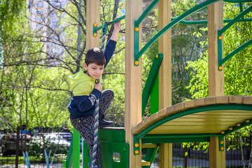 Teenager boy climbing at kid playground outdoor. The climber trains simulator on the street....