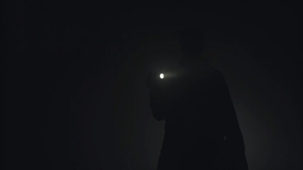Silhouette of man shining with flashlight in the dark. Stock footage. Silhouette of man in thick fog