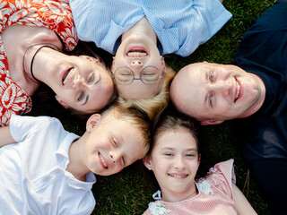 The family lies on the lawn in the recreation park with their heads to each other, look up and laugh. The concept of well-being in the family. top camera