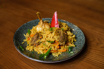 dish of cooked pilaff with rice and meat on plate with head of garlic, pepper and greens on brown...