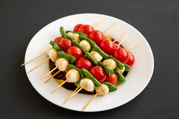 Homemade caprese skewer appetizer on a plate on a black background, side view.