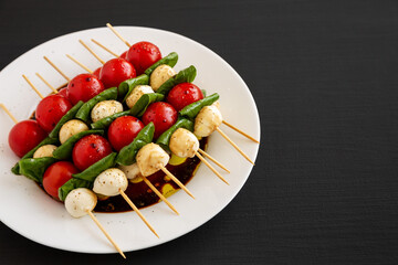 Homemade caprese skewer appetizer on a plate on a black surface, side view. Copy space.