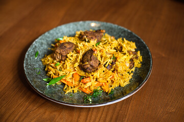 dish of cooked pilaf with rice, meat, vegetables and greens on plate on brown wooden background