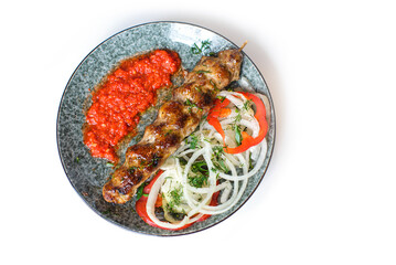 roasted kebab served with tomato sauce, onion and pepper rings on plate on white background flatlay