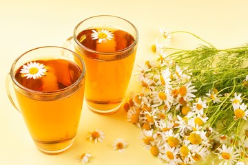 Transparent mugs with a drink (tea, decoction) of useful chamomile pharmacy (medicinal) on a yellow background. Phytotherapy, herbal tea.